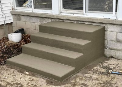 Freshly poured concrete steps leading to a glass door of a house, with construction materials nearby.