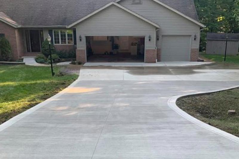 A clean, newly-paved concrete driveway leads to a two-car garage of a suburban house.