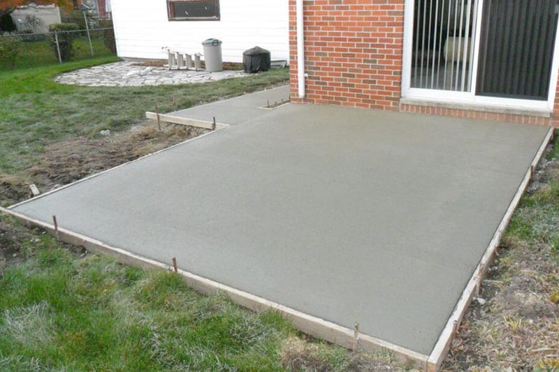 Freshly poured concrete patio next to a house with brick and sliding glass doors, still framed by wooden boards.