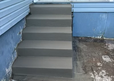 Freshly poured concrete steps leading up to a sliding glass door beside a blue house.