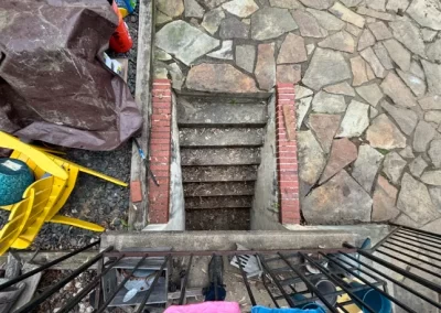 View of stone steps leading down to a basement, surrounded by brick and cluttered outdoor items.