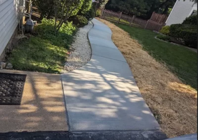Freshly poured, winding concrete sidewalk bordered by grass, mulch, and landscaping beside a house.