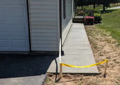 Fresh concrete sidewalk beside a house, marked off with yellow caution tape, leading to a porch.