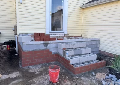 Partially built brick steps leading to a door, with construction materials and tools around.