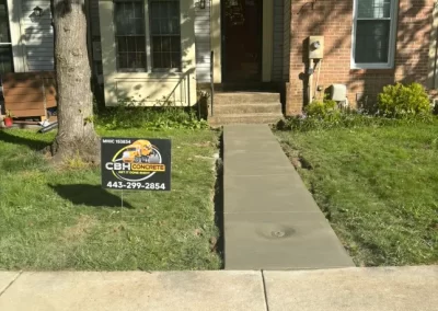 Freshly poured concrete sidewalk leading to a townhouse, with a CBH Concrete sign on the lawn.