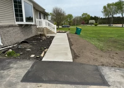 Freshly poured concrete sidewalk leading to a house, surrounded by soil and a grassy yard.