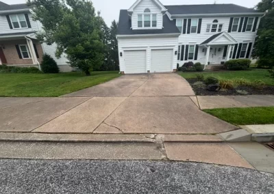A driveway with a large crack leading to a white two-car garage of a suburban house.