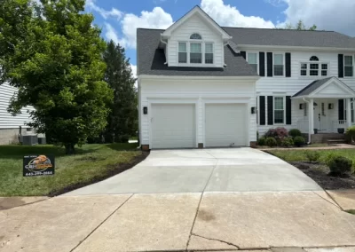 White house with double garage and fresh concrete driveway, tree on left, contractor sign on lawn.