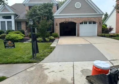 Freshly poured concrete driveway in front of a brick house, with a lawn sign and orange cooler visible.