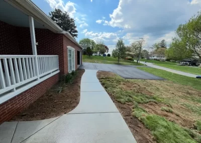 Freshly poured sidewalk curves from a brick house's porch to a driveway on a sunny day.