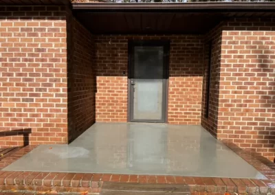 A brick house entrance with a wet, freshly poured concrete porch and a glass door.