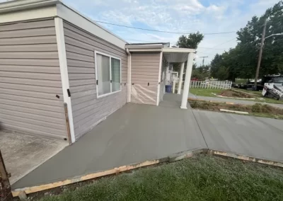 Freshly poured concrete sidewalk and porch area in front of a beige house with white trim.