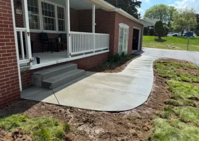 Freshly poured concrete sidewalk curves from driveway to the front porch of a brick house.