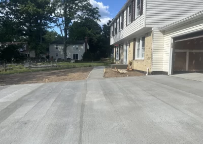 Freshly poured concrete driveway and sidewalk in front of a house, with a garage and yard visible.