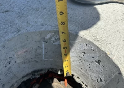 A tape measure shows a depth of about 10 inches in a hole on a concrete surface next to a sneaker.