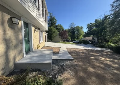 Freshly poured concrete walkway and driveway in front of a house on a sunny day, with green trees in view.