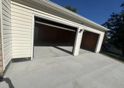Two-car garage with both doors open, empty interior, and a clean concrete driveway on a sunny day.