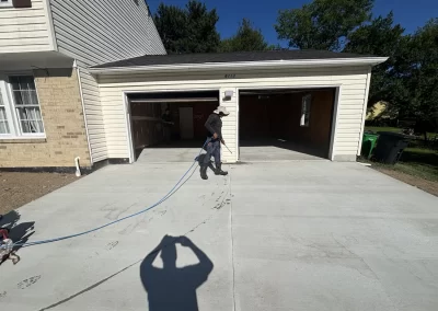 Person power washing a driveway in front of a two-car garage on a sunny day.