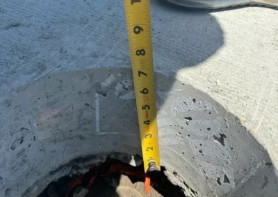 A tape measure shows a depth of about 7 inches in a hole on a concrete surface next to a sneaker.